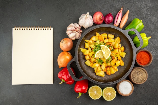 Vista superior de papas fritas dentro de la sartén con diferentes condimentos y verduras en el fondo oscuro