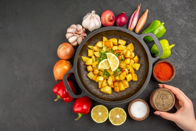 Vista superior de papas fritas dentro de la sartén con diferentes condimentos y verduras en el fondo oscuro