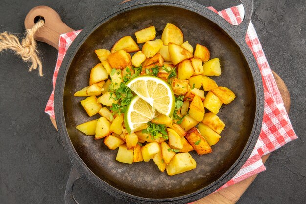 Vista superior de papas fritas dentro de la sartén con verduras y limón sobre el fondo oscuro