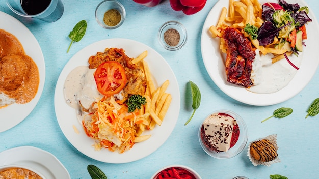 Vista superior de papas fritas con ensaladas, carne asada y salsas en la mesa