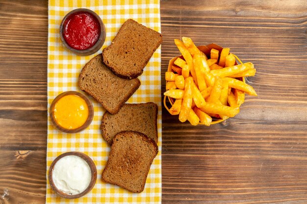 Vista superior de papas fritas con hogazas de pan oscuro en la comida de hamburguesa de comida de pan de patata de mesa marrón