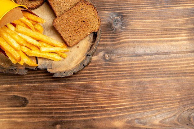 Vista superior de papas fritas con hogazas de pan oscuro en la mesa marrón