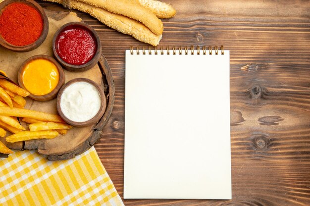 Vista superior de papas fritas con pan y condimentos en la mesa de madera marrón comida rápida patata pimienta picante