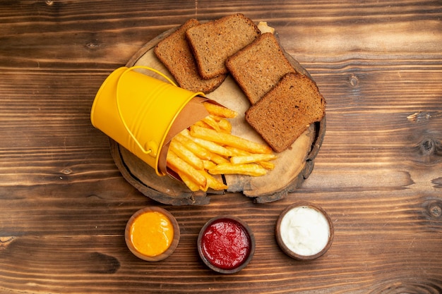 Vista superior de papas fritas con pan oscuro y condimentos en mesa marrón