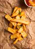 Foto gratuita vista superior de papas fritas en papel con hierbas y salsa de tomate