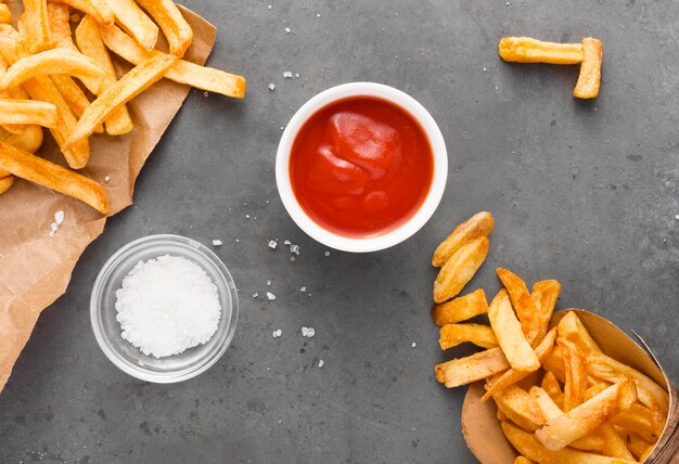 Vista superior de papas fritas en papel con sal y salsa de tomate