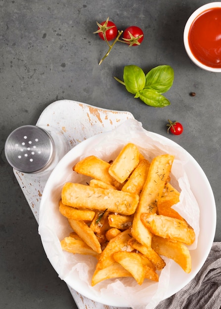 Vista superior de papas fritas en un plato con salero y salsa de tomate