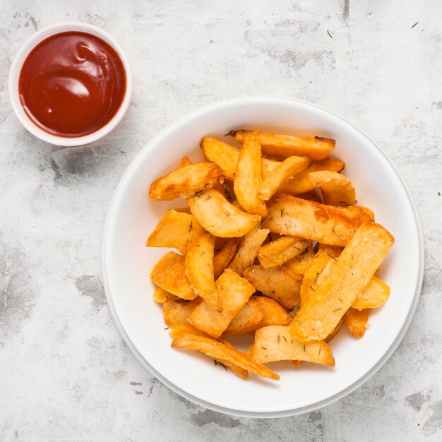 Vista superior de papas fritas saladas en un plato con salsa de tomate