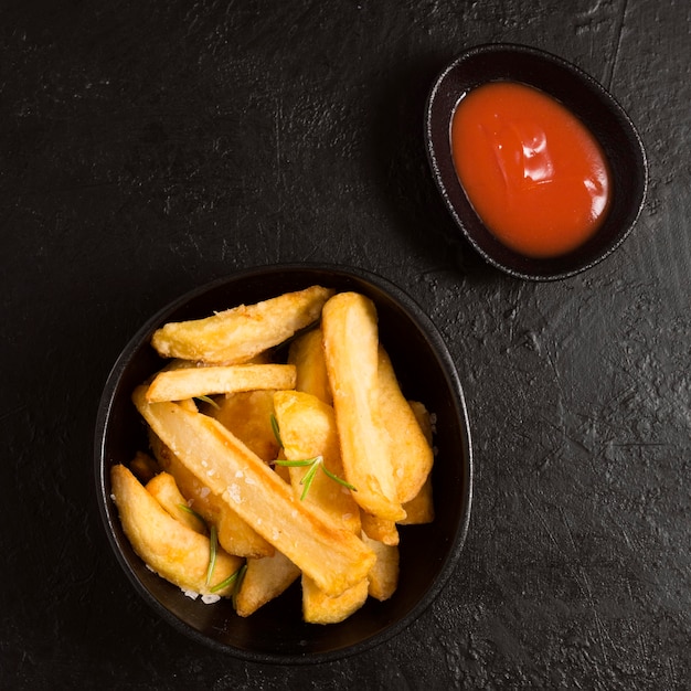 Vista superior de papas fritas en un tazón con salsa de tomate