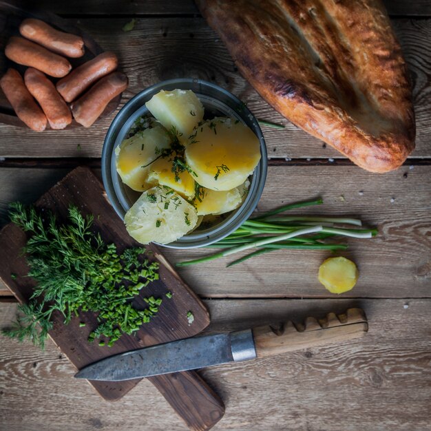 Vista superior de papas hervidas con cebolla verde y pan y cuchillo en la mesa