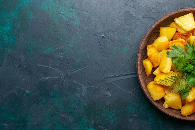 Vista superior de papas en rodajas cocidas con verduras dentro de la placa marrón en el escritorio azul oscuro