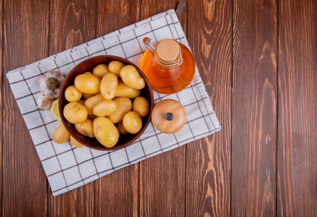 Vista superior de papas en un tazón con ajo, limón, sal y mantequilla sobre tela escocesa y madera con espacio de copia