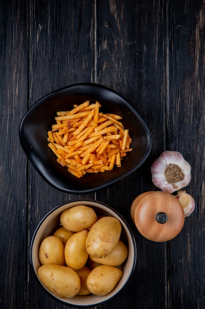 Foto gratuita vista superior de papas en tazones como enteros fritos y crudos con sal y ajo sobre madera