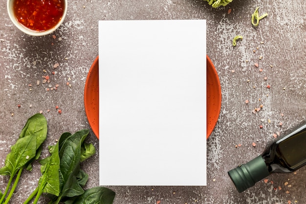 Vista superior del papel de menú en blanco en un plato con espinacas y aceite de oliva