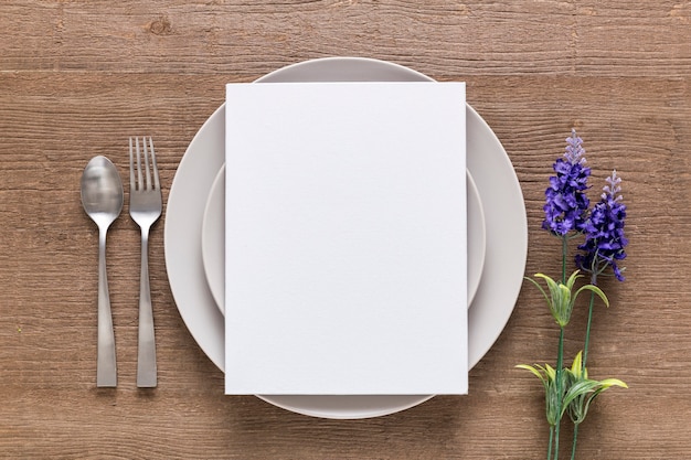 Vista superior del papel de menú en blanco en un plato con flores y cubiertos