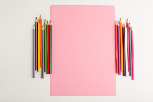 Vista superior de papel rosa en blanco con lápices de colores sobre superficie blanca