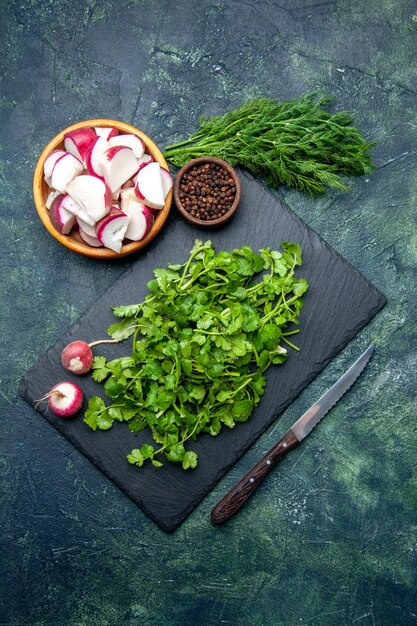 Vista superior del paquete de cilantro pimiento de rábanos picados enteros frescos en una tabla de cortar de madera y un cuchillo sobre fondo verde negro de colores mezclados con espacio libre