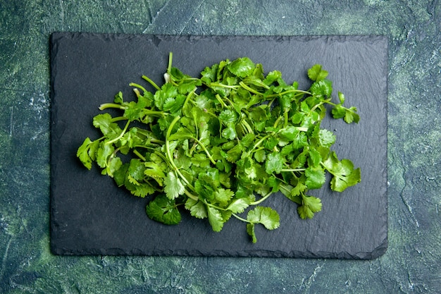 Vista superior del paquete de cilantro sobre tabla de cortar de madera sobre fondo verde negro de colores mezclados con espacio libre