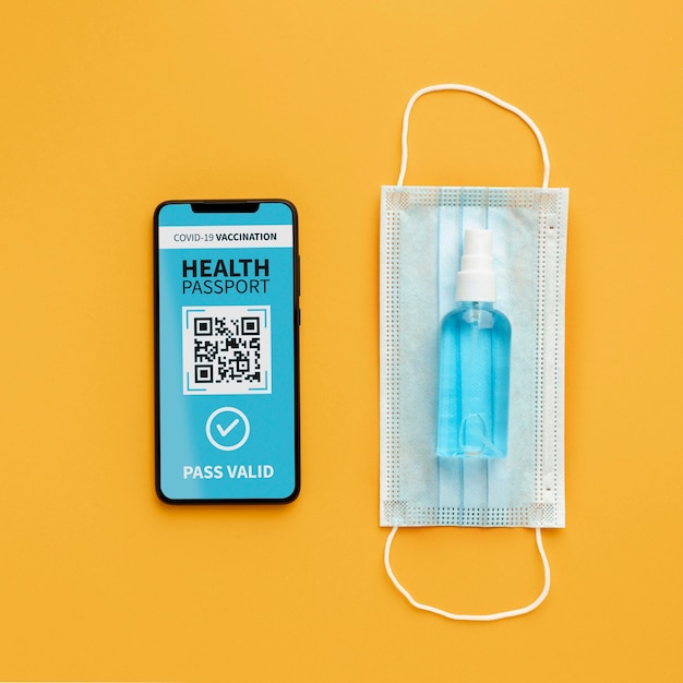 Vista superior del pasaporte de salud virtual en un teléfono inteligente con mascarilla médica y desinfectante para manos