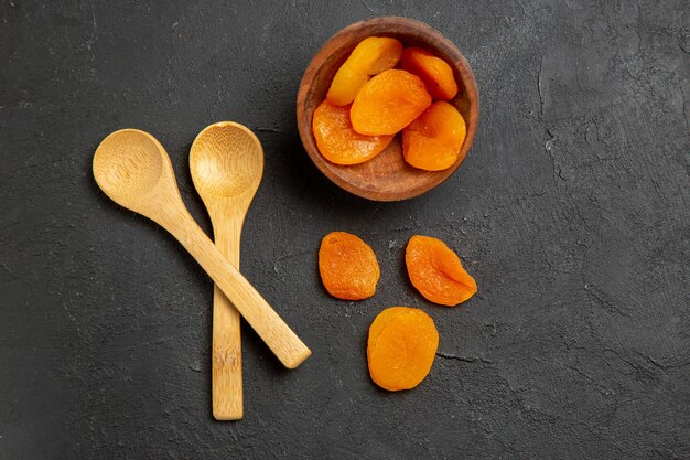 Vista superior pasas de albaricoque seco con cucharas de madera sobre pasas de frutos secos de superficie oscura