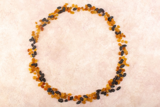 Una vista superior de pasas secas de naranja con frutos secos negros formando un círculo en rosa