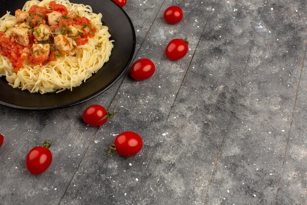 Vista superior pasta cocinada con alitas de pollo y salsa de tomate dentro de la placa negra sobre el fondo gris de madera rústica