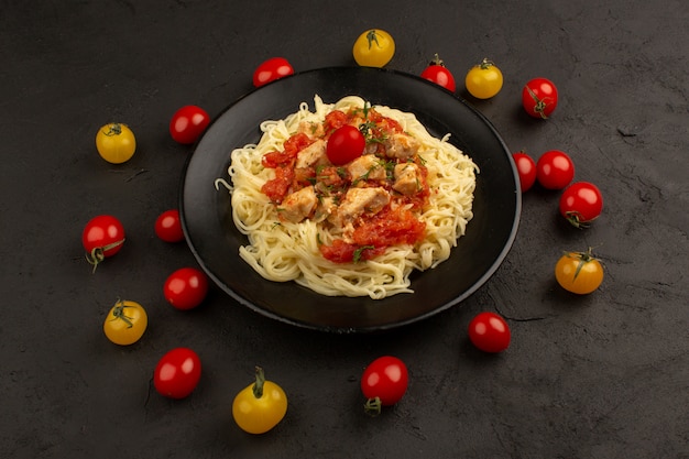 Vista superior pasta cocinada con trozos de pollo y salsa de tomate dentro de un plato negro en la oscuridad