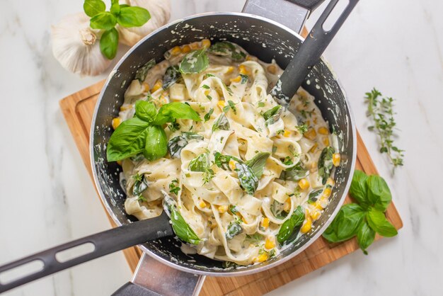 Vista superior de pasta cremosa de tagliatelle con hierbas y maíz en una olla sobre la mesa