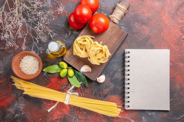 Foto gratuita vista superior de pasta cruda con aceite y tomates en pasta de superficie oscura pasta cruda