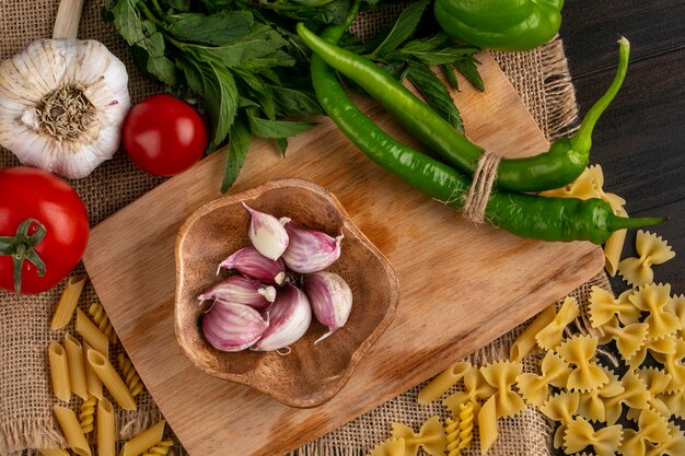 Vista superior de pasta cruda con ajo y chiles en una tabla de cortar con tomates y un manojo de menta en una servilleta beige