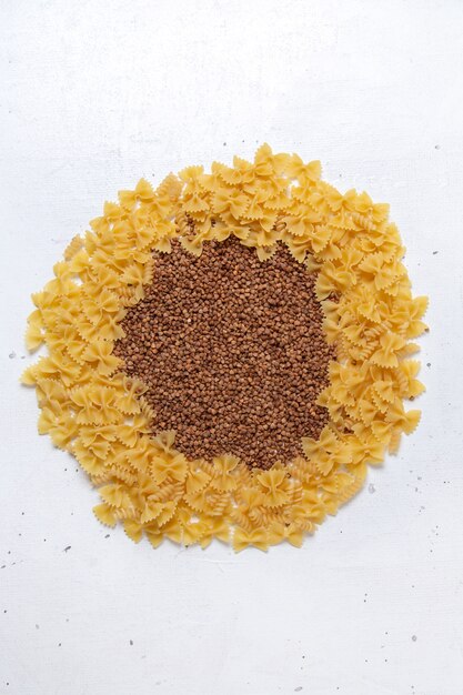 Vista superior de pasta cruda amarilla poco formada con trigo sarraceno en el escritorio blanco pasta comida italiana