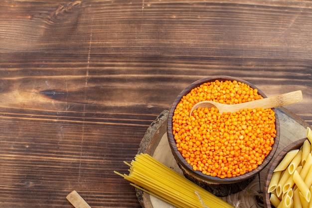 Vista superior de pasta cruda con lentejas naranjas sobre superficie rústica de madera marrón