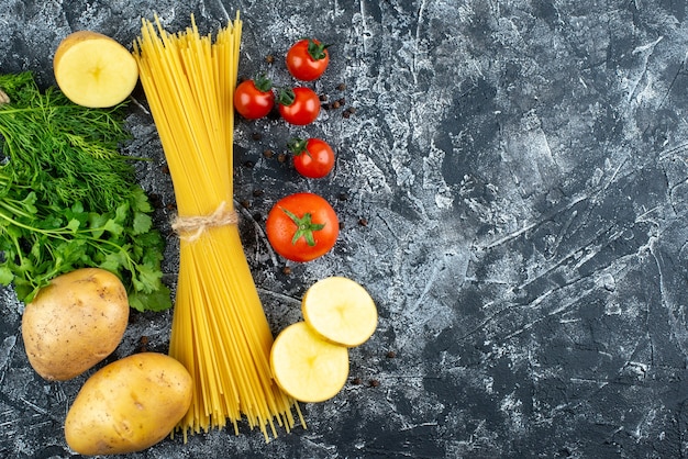 Vista superior de pasta cruda con patata, perejil y tomates en superficie gris claro