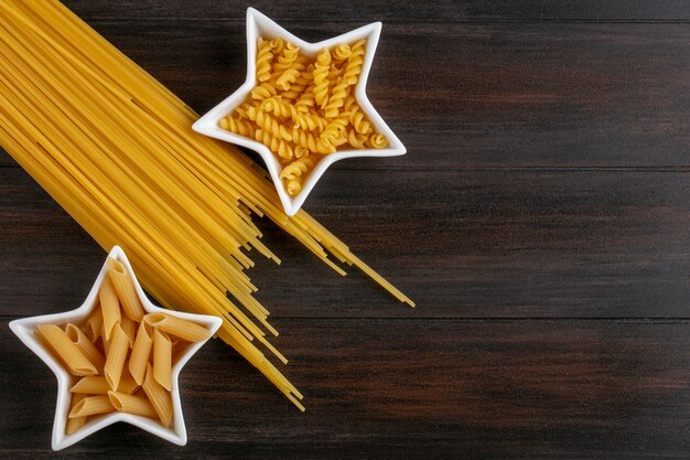 Vista superior de la pasta cruda en platillos en forma de estrella con espaguetis crudos sobre una superficie de madera