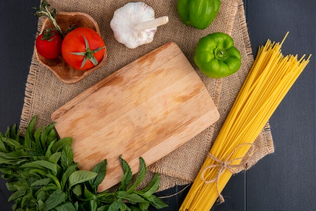 Vista superior de pasta cruda con tabla de cortar tomates ajo menta y pimiento en una servilleta beige