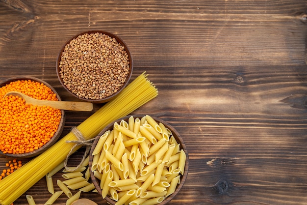 Vista superior de pasta cruda con trigo sarraceno y lentejas sobre superficie marrón