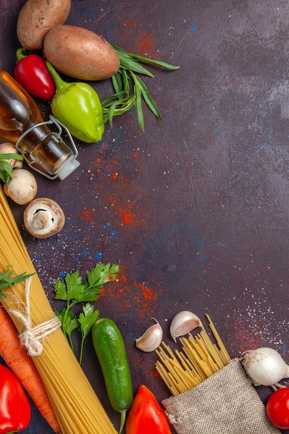 Vista superior de pasta cruda con verduras frescas en comida de ensalada de superficie oscura