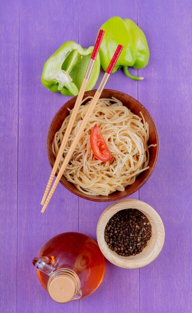 Vista superior de pasta de espagueti con rodaja de tomate y palillos en un tazón con medio pimiento pimienta negra mantequilla derretida sobre fondo morado