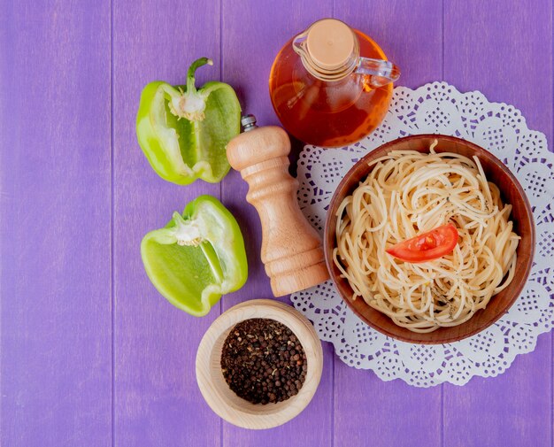 Vista superior de pasta de espagueti en un tazón sobre tapete de papel con sal de mantequilla de pimienta a medio cortar y pimienta negra en la mesa morada