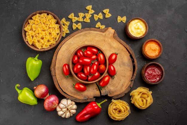 Vista superior de la pasta de especias en un tazón tres tipos de salsa ajo cebolla pimiento rojo y verde junto a los tomates en la tabla de cortar de madera