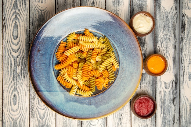 Vista superior de pasta espiral cocida con diferentes condimentos en el escritorio gris pasta color pimienta comida