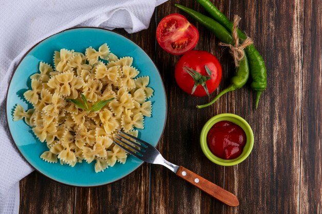 Vista superior de la pasta hervida en una placa azul con un tenedor de tomate ketchup y chiles sobre una superficie de madera