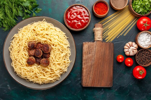 Vista superior de pasta italiana cocida con albóndigas y diferentes condimentos en la superficie azul oscuro