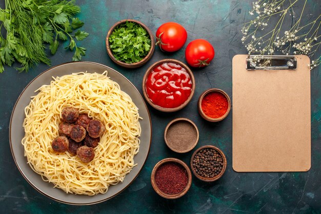 Vista superior de pasta italiana cocida con albóndigas y diferentes condimentos en la superficie azul