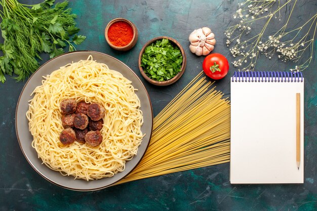 Vista superior de pasta italiana cocida con albóndigas y verduras en la superficie azul oscuro