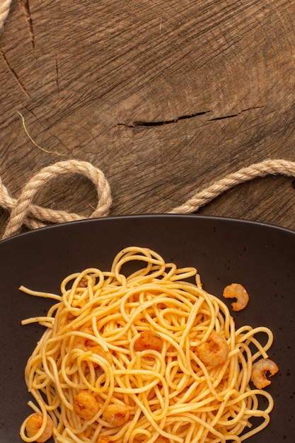 Vista superior de pasta italiana cocida con camarones dentro de placa marrón con cuerdas en el escritorio de madera