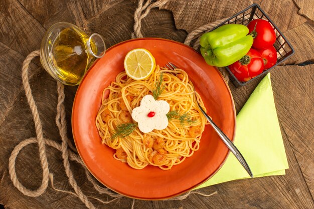 Vista superior de pasta italiana cocida con camarones verdes y rodajas de limón junto con verduras y aceite dentro de la placa naranja