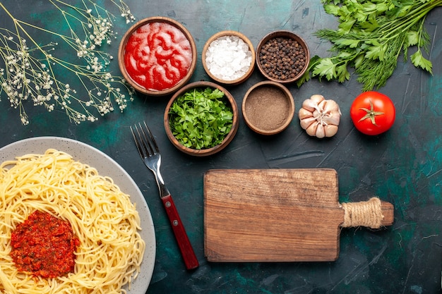 Vista superior de pasta italiana cocida con carne y diferentes condimentos en la superficie azul