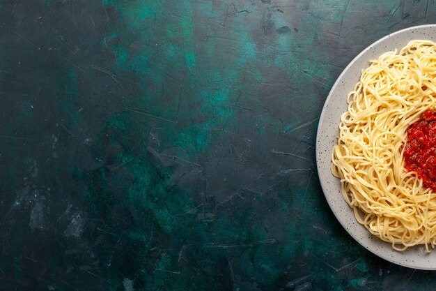 Vista superior de pasta italiana cocida con carne picada y salsa de tomate en el escritorio azul oscuro