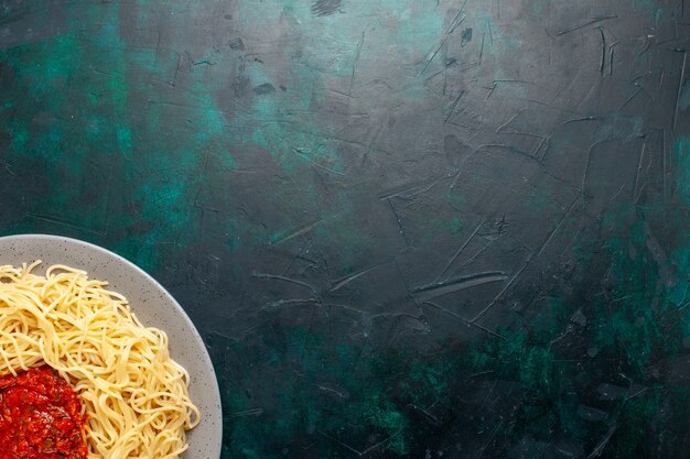 Vista superior de pasta italiana cocida con carne picada y salsa de tomate sobre la superficie azul oscuro